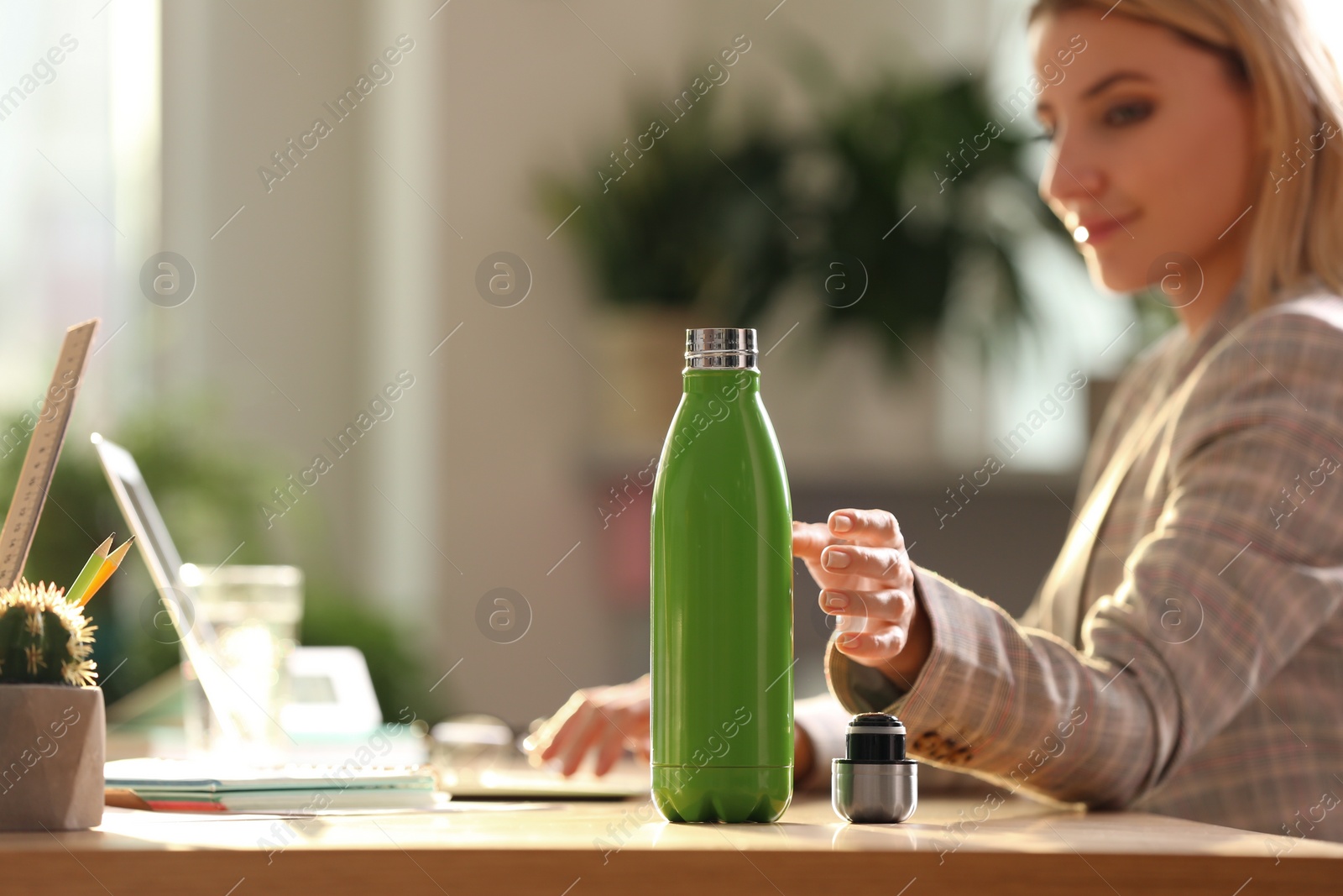 Woman taking green thermos bottle at workplace, closeup Photo of Woman taking green thermos bottle at workplace, closeup