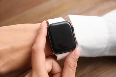 Woman checking stylish smart watch at wooden table, closeup Image of Woman checking stylish smart watch at wooden table, closeup