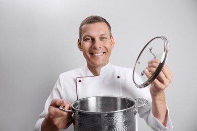 Happy male chef with cooking pot on light grey background Photo of Happy male chef with cooking pot on light grey background