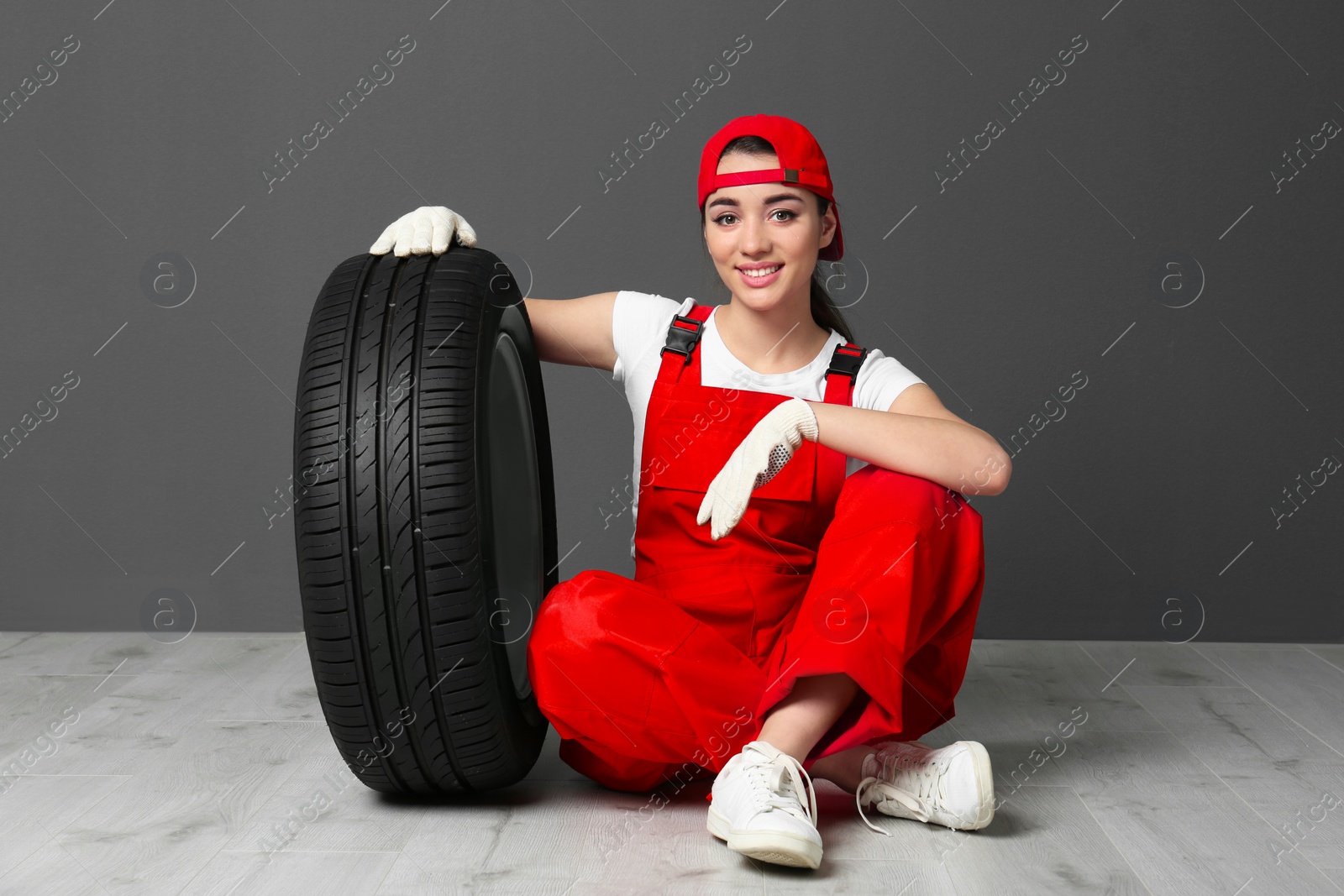 Female mechanic in uniform with car tire on grey wall background Photo of Female mechanic in uniform with car tire on grey wall background