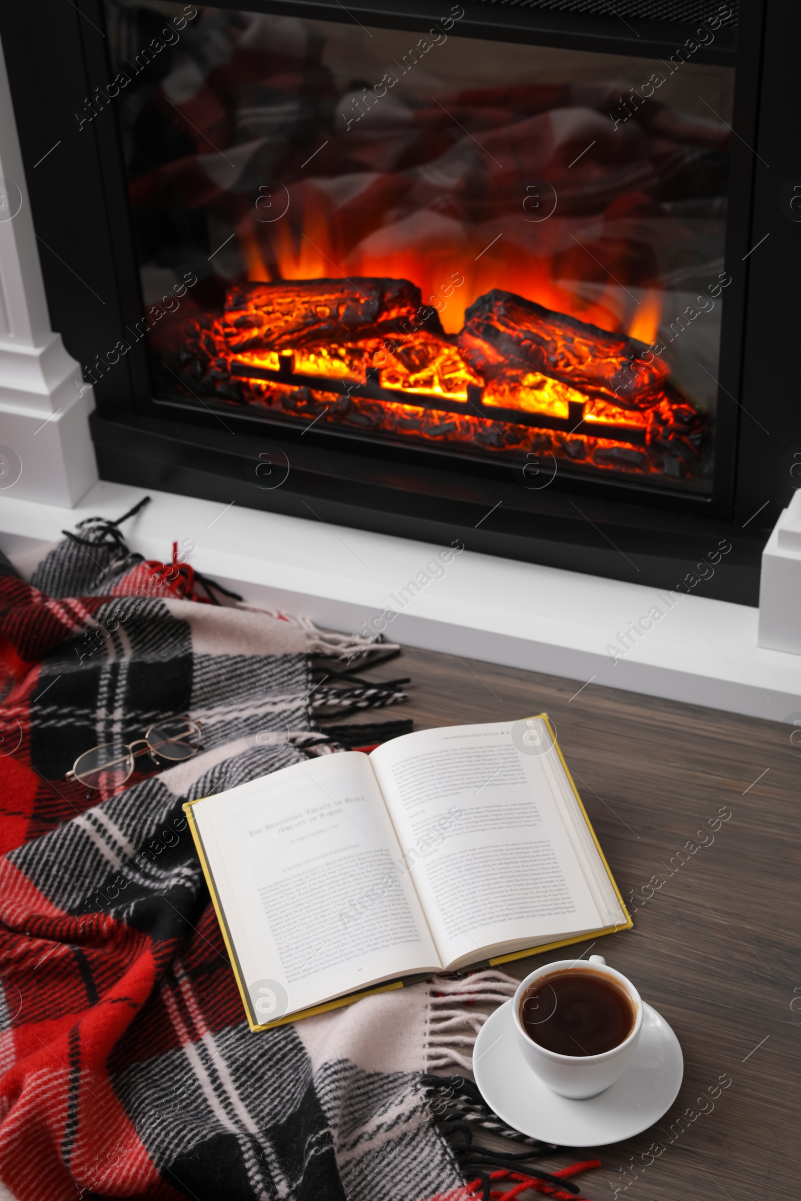 Cup of hot coffee, plaid and book on floor near fireplace, above view. Cozy atmosphere Photo of Cup of hot coffee, plaid and book on floor near fireplace, above view. Cozy atmosphere