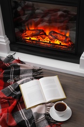 Cup of hot coffee, plaid and book on floor near fireplace, above view. Cozy atmosphere Photo of Cup of hot coffee, plaid and book on floor near fireplace, above view. Cozy atmosphere