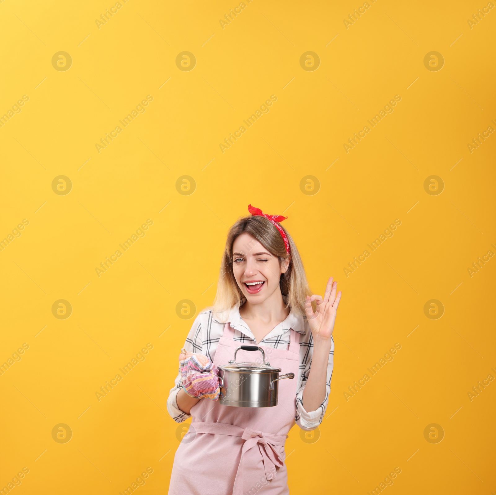 Young housewife with pot on yellow background Photo of Young housewife with pot on yellow background