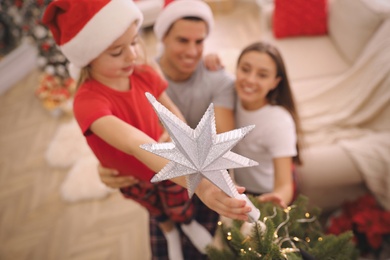 Family decorating Christmas tree indoors, focus on star topper Photo of Family decorating Christmas tree indoors, focus on star topper