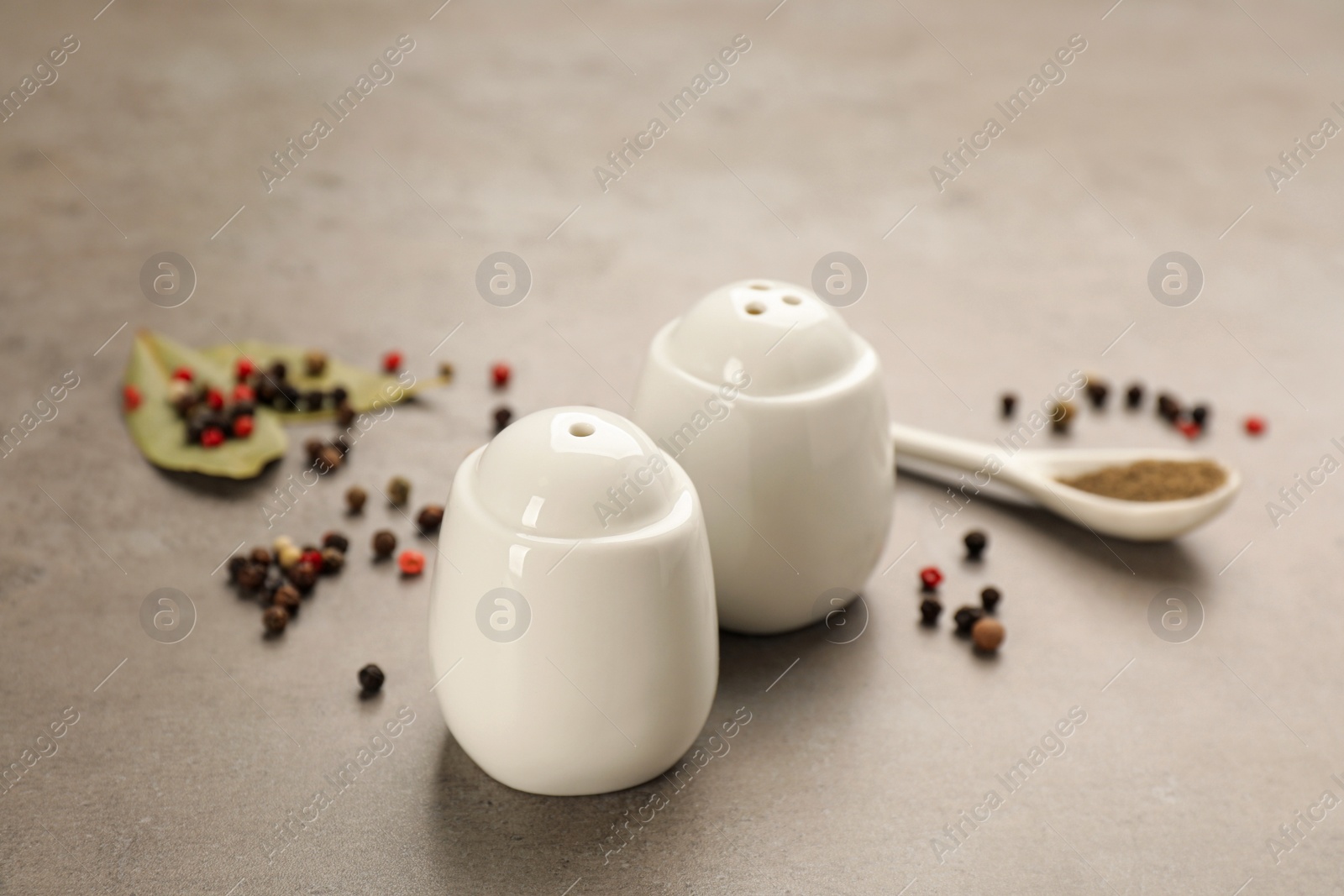 White ceramic salt and pepper shakers, bay leaves with spoon on light table, closeup Photo of White ceramic salt and pepper shakers, bay leaves with spoon on light table, closeup