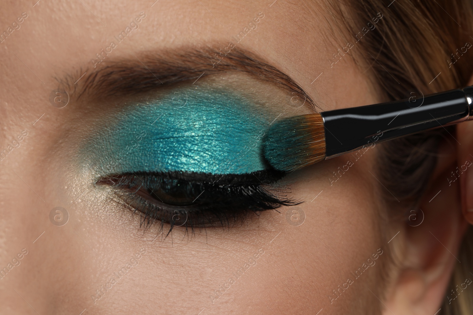 Applying cyan eye shadow onto woman's face, closeup. Beautiful evening makeup Photo of Applying cyan eye shadow onto woman's face, closeup. Beautiful evening makeup