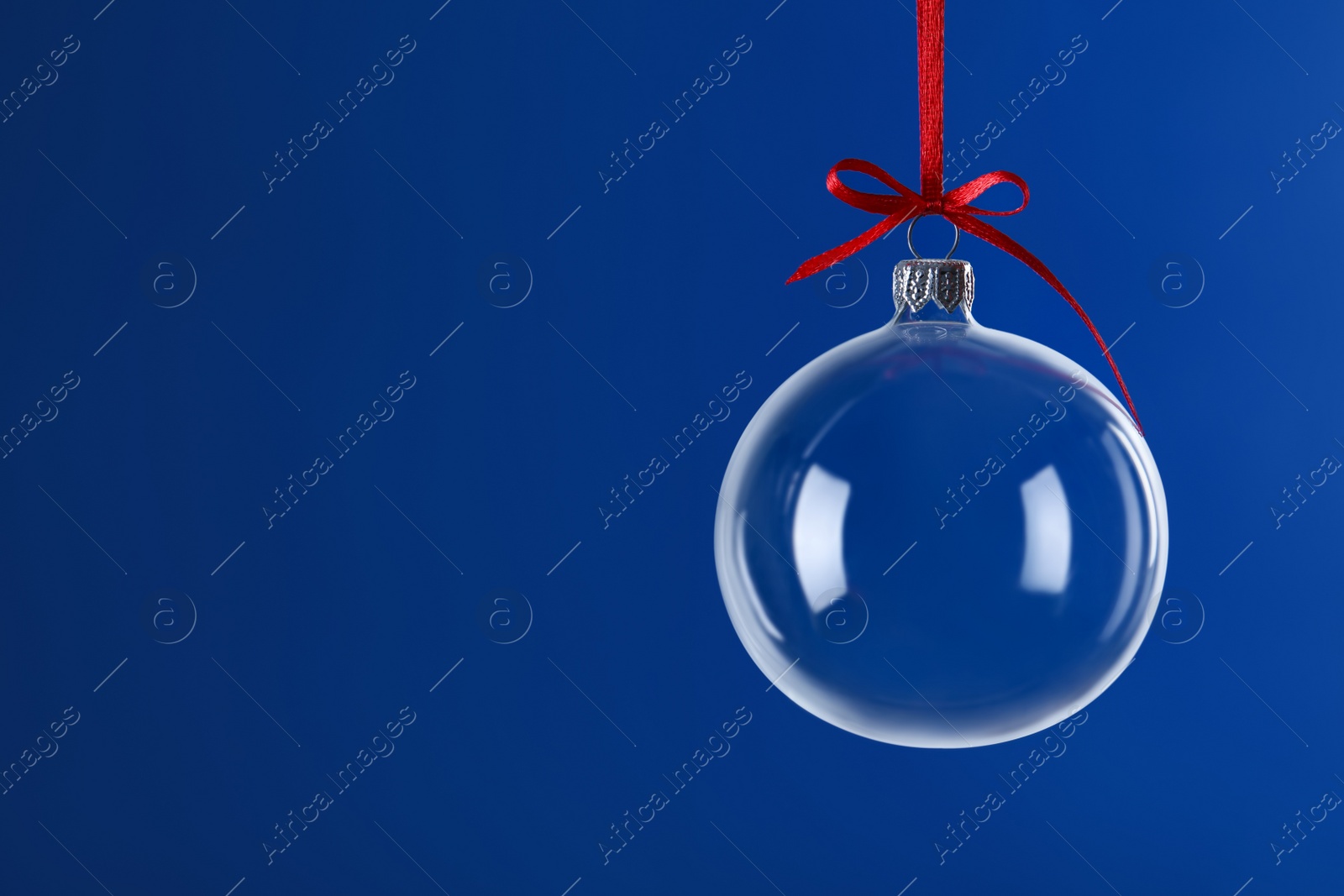 Transparent glass Christmas ball with red ribbon and bow against blue background. Space for text Photo of Transparent glass Christmas ball with red ribbon and bow against blue background. Space for text