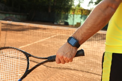 Man wearing modern smart watch during training on tennis court, closeup Photo of Man wearing modern smart watch during training on tennis court, closeup