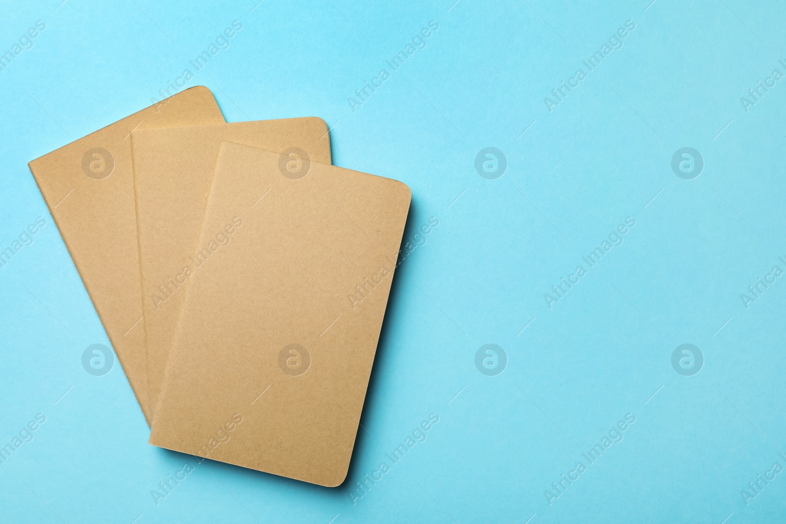 Photo of Stylish kraft planners on light blue background, flat lay. Space for text
