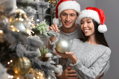 Happy young couple in Santa hats decorating Christmas tree together at home Photo of Happy young couple in Santa hats decorating Christmas tree together at home
