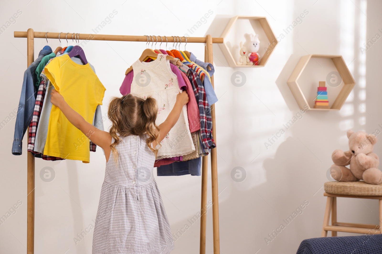 Little girl choosing clothes on rack in room Photo of Little girl choosing clothes on rack in room
