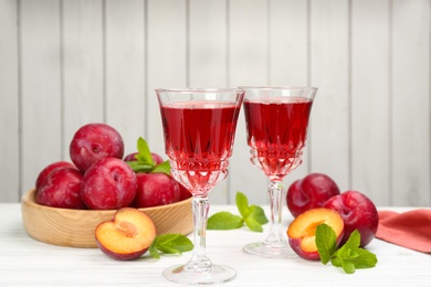 Delicious plum liquor, ripe fruits and mint on table against white background. Homemade strong alcoholic beverage Photo of Delicious plum liquor, ripe fruits and mint on table against white background. Homemade strong alcoholic beverage