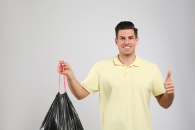 Photo of Man holding full garbage bag on light background
