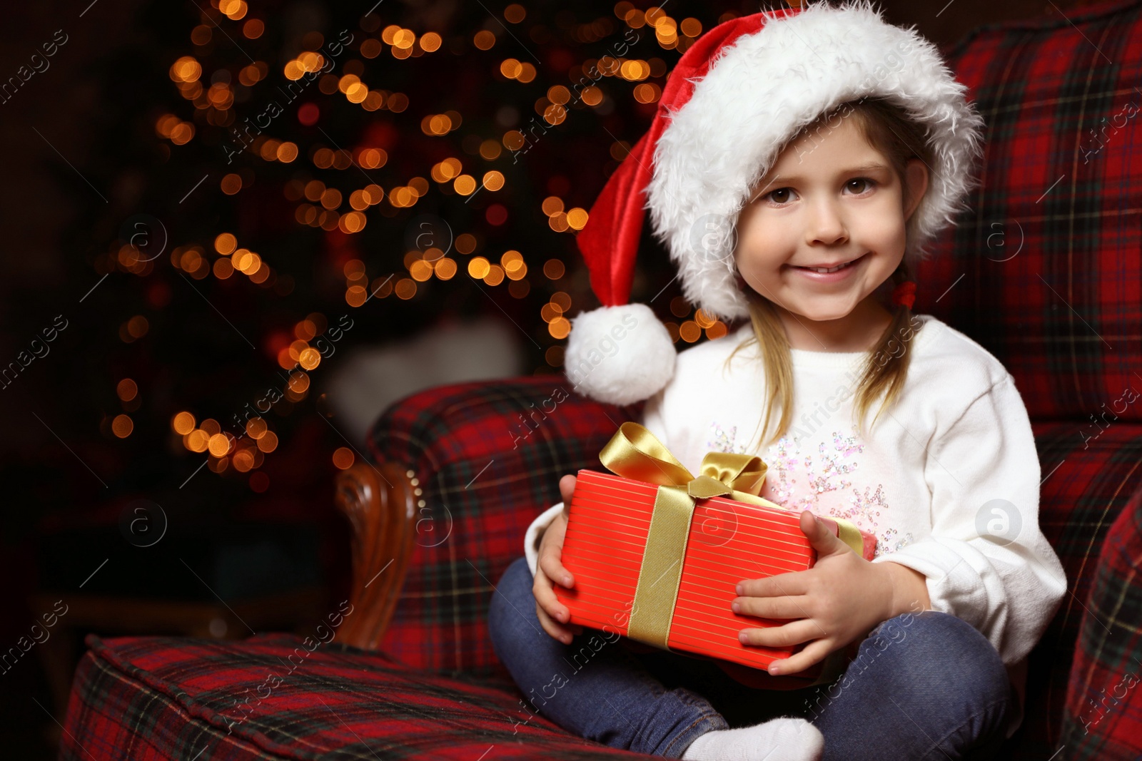 Cute little child with Christmas gift sitting in armchair at home Photo of Cute little child with Christmas gift sitting in armchair at home