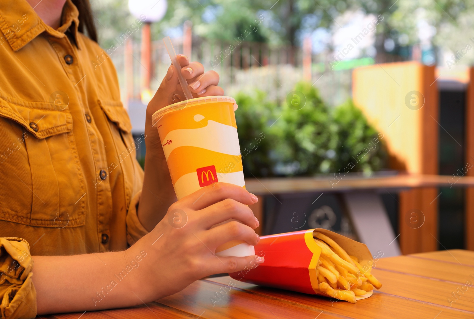 MYKOLAIV, UKRAINE - AUGUST 11, 2021: Woman with cold McDonald's drink and French fries outdoors, closeup Photo of MYKOLAIV, UKRAINE - AUGUST 11, 2021: Woman with cold McDonald's drink and French fries outdoors, closeup