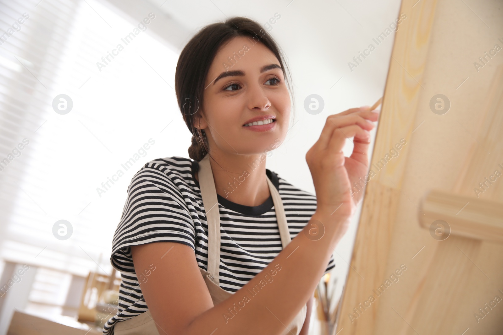 Young woman drawing on canvas with brush indoors Photo of Young woman drawing on canvas with brush indoors