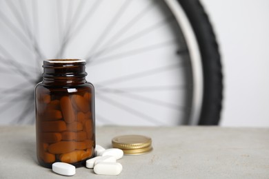 Pills on light grey table near bike wheel, space for text. Using doping in cycling sport concept Photo of Pills on light grey table near bike wheel, space for text. Using doping in cycling sport concept