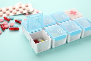Plastic box with different pills on turquoise background, closeup Photo of Plastic box with different pills on turquoise background, closeup