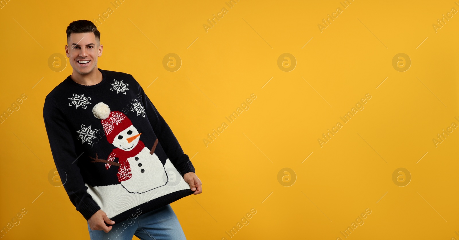 Happy man showing his Christmas sweater on yellow background Photo of Happy man showing his Christmas sweater on yellow background
