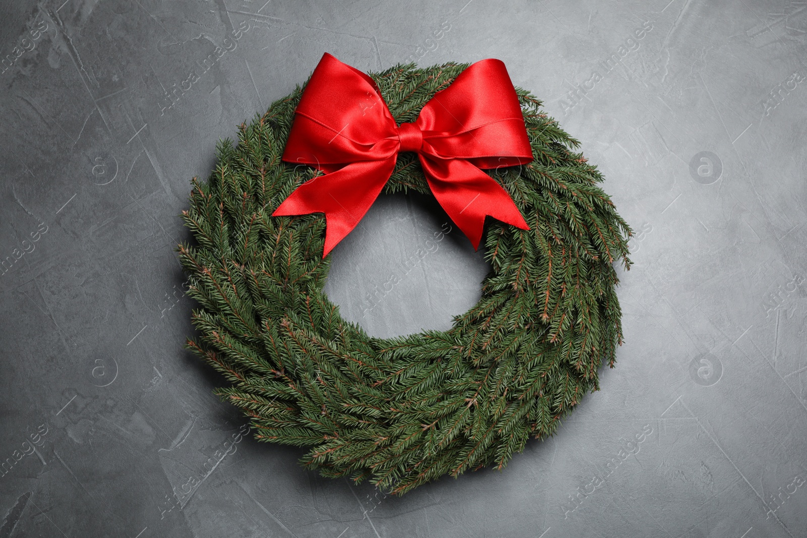 Christmas wreath made of fir branches with red bow on grey background, top view Photo of Christmas wreath made of fir branches with red bow on grey background, top view