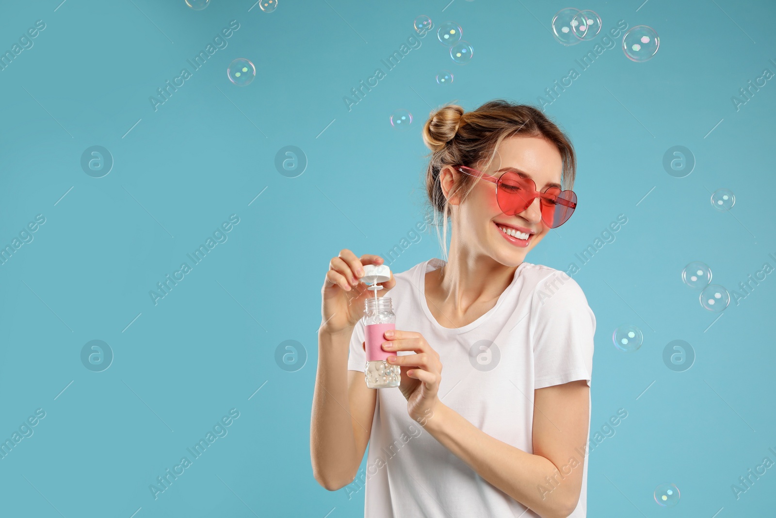 Young woman blowing soap bubbles on light blue background, space for text Photo of Young woman blowing soap bubbles on light blue background, space for text