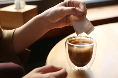 Photo of Woman adding sugar to aromatic coffee at table in cafe, closeup