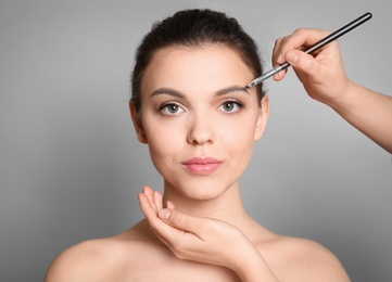 Visage artist applying makeup on woman's face against grey background. Professional cosmetic products Photo of Visage artist applying makeup on woman's face against grey background. Professional cosmetic products
