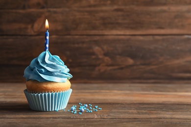 Delicious birthday cupcake with burning candle on wooden table Photo of Delicious birthday cupcake with burning candle on wooden table