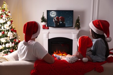 Family watching festive movie on TV in room decorated for Christmas, back view Image of Family watching festive movie on TV in room decorated for Christmas, back view