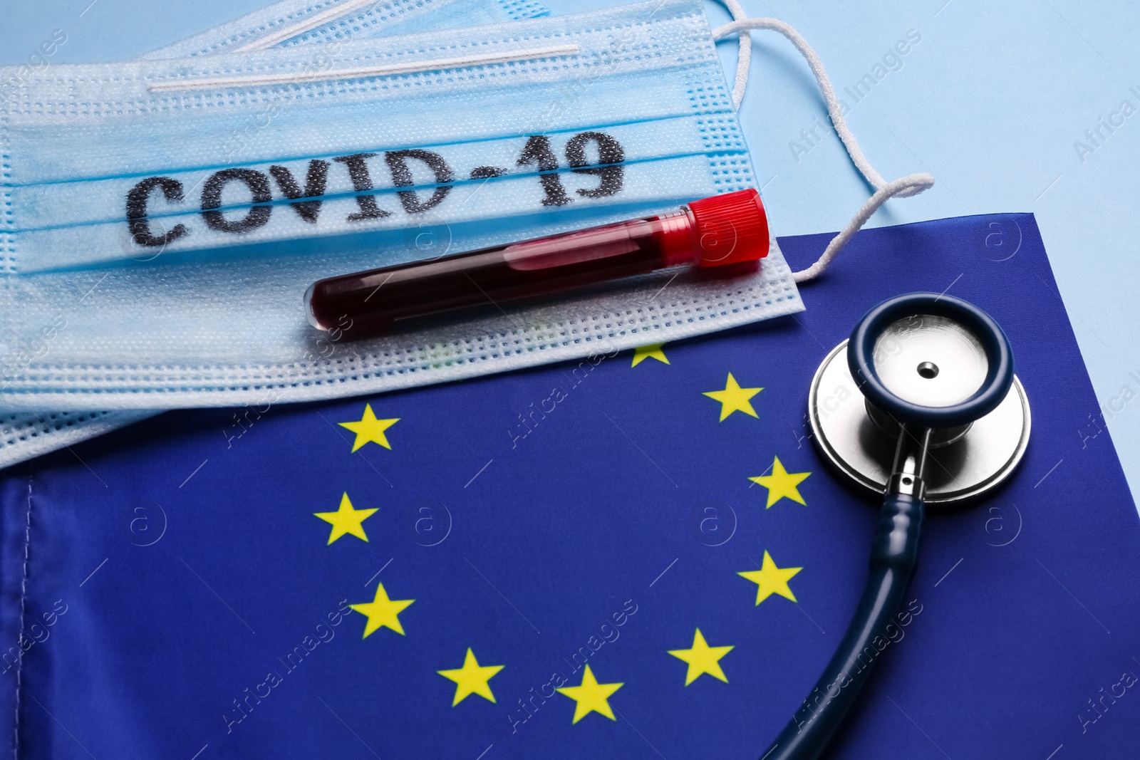 European Union flag, protective masks and test tube with blood sample on light blue background. Coronavirus outbreak Photo of European Union flag, protective masks and test tube with blood sample on light blue background. Coronavirus outbreak