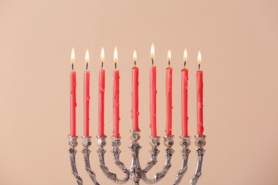 Silver menorah with burning candles on beige background. Hanukkah celebration Photo of Silver menorah with burning candles on beige background. Hanukkah celebration