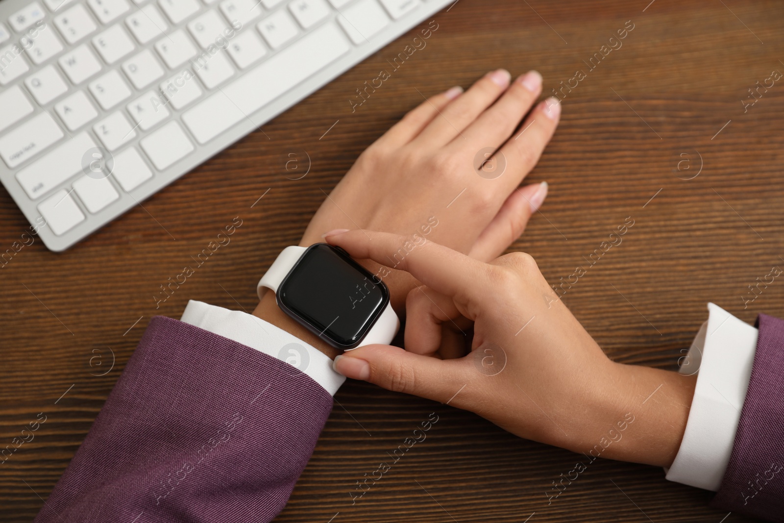 Woman using stylish smart watch at wooden table, closeup Image of Woman using stylish smart watch at wooden table, closeup