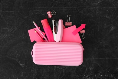 Pink pencil case and different stationery on blackboard, flat lay. Back to school Photo of Pink pencil case and different stationery on blackboard, flat lay. Back to school