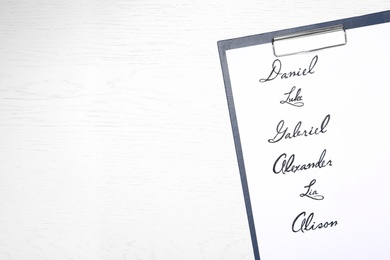 Clipboard with written different baby names on white wooden table, top view. Space for text Photo of Clipboard with written different baby names on white wooden table, top view. Space for text