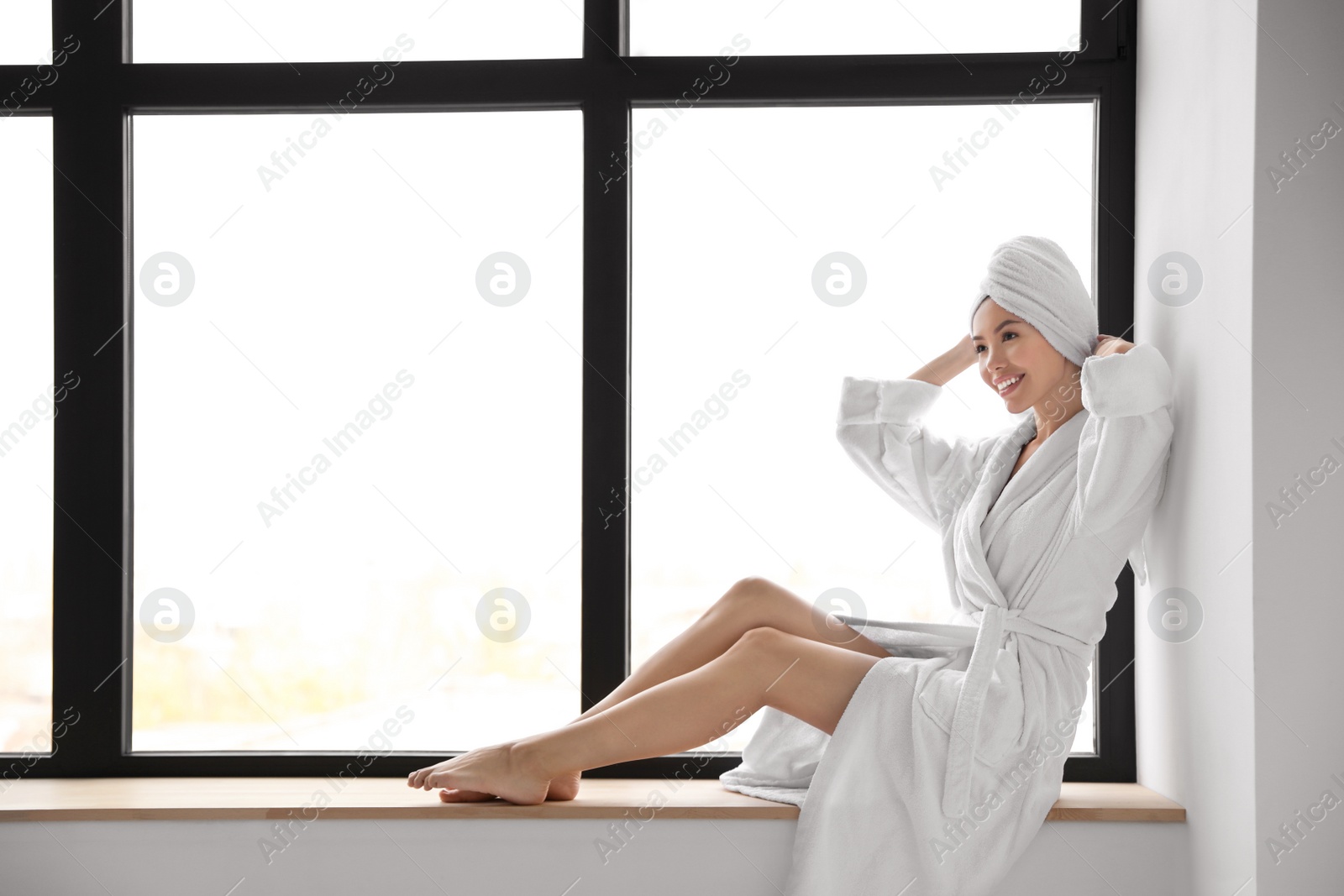 Photo of Young woman with towel wearing bathrobe near window