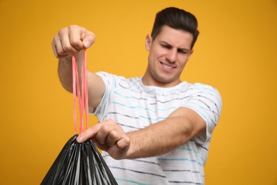 Man holding full garbage bag against yellow background, focus on hands Photo of Man holding full garbage bag against yellow background, focus on hands