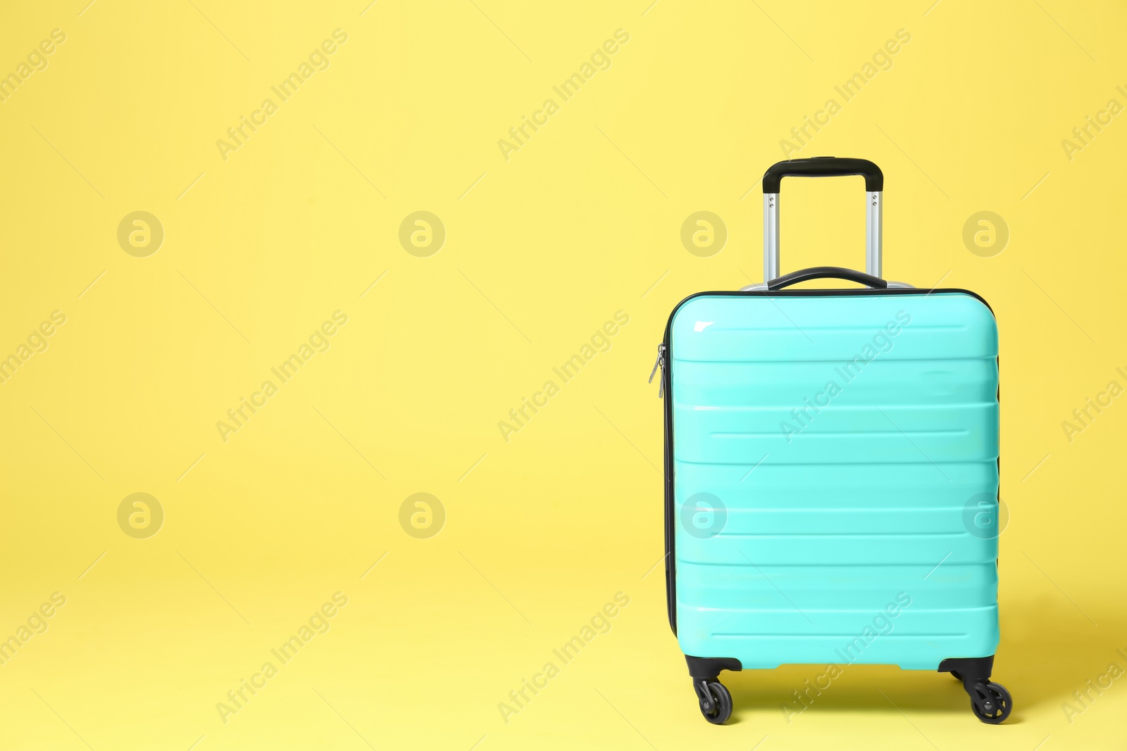 Photo of Stylish turquoise suitcase on yellow background. Space for text