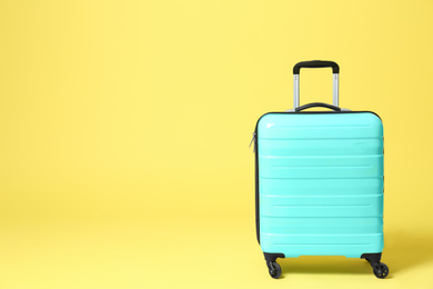 Stylish turquoise suitcase on yellow background. Space for text Photo of Stylish turquoise suitcase on yellow background. Space for text
