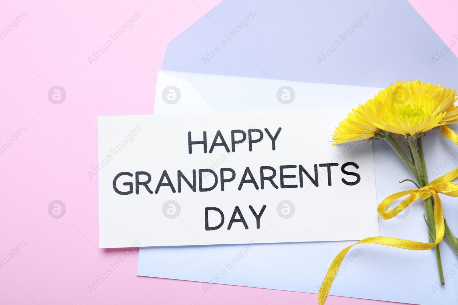 Card with phrase Happy Grandparents Day, envelope and beautiful flowers on pink background, flat lay Photo of Card with phrase Happy Grandparents Day, envelope and beautiful flowers on pink background, flat lay