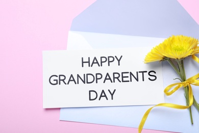 Card with phrase Happy Grandparents Day, envelope and beautiful flowers on pink background, flat lay Photo of Card with phrase Happy Grandparents Day, envelope and beautiful flowers on pink background, flat lay