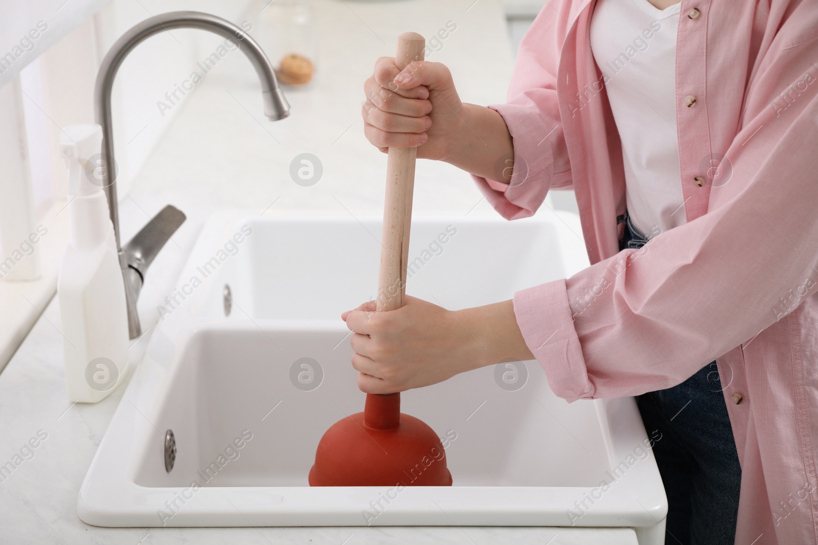 Woman using plunger to unclog sink drain in kitchen, closeup Photo of Woman using plunger to unclog sink drain in kitchen, closeup