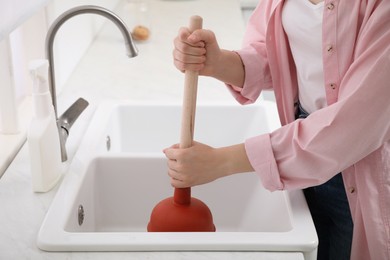 Woman using plunger to unclog sink drain in kitchen, closeup Photo of Woman using plunger to unclog sink drain in kitchen, closeup
