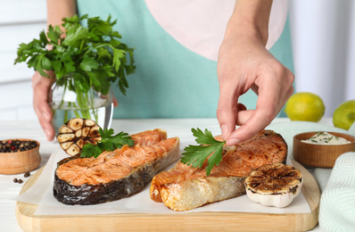 Woman adding parsley to cooked red fish on white wooden table, closeup Photo of Woman adding parsley to cooked red fish on white wooden table, closeup