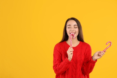 Young woman in red sweater holding candy canes on yellow background, space for text. Celebrating Christmas Photo of Young woman in red sweater holding candy canes on yellow background, space for text. Celebrating Christmas