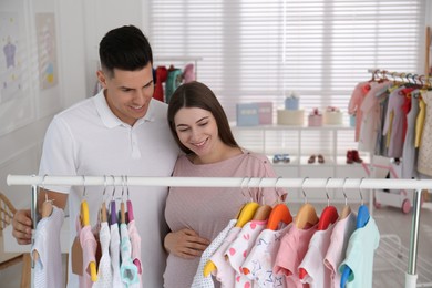 Happy pregnant woman with her husband choosing baby clothes in store. Shopping concept Photo of Happy pregnant woman with her husband choosing baby clothes in store. Shopping concept