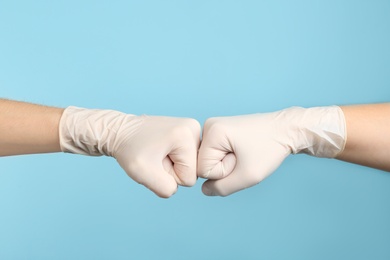 People in medical gloves doing fist bump on light blue background, closeup of hands Photo of People in medical gloves doing fist bump on light blue background, closeup of hands