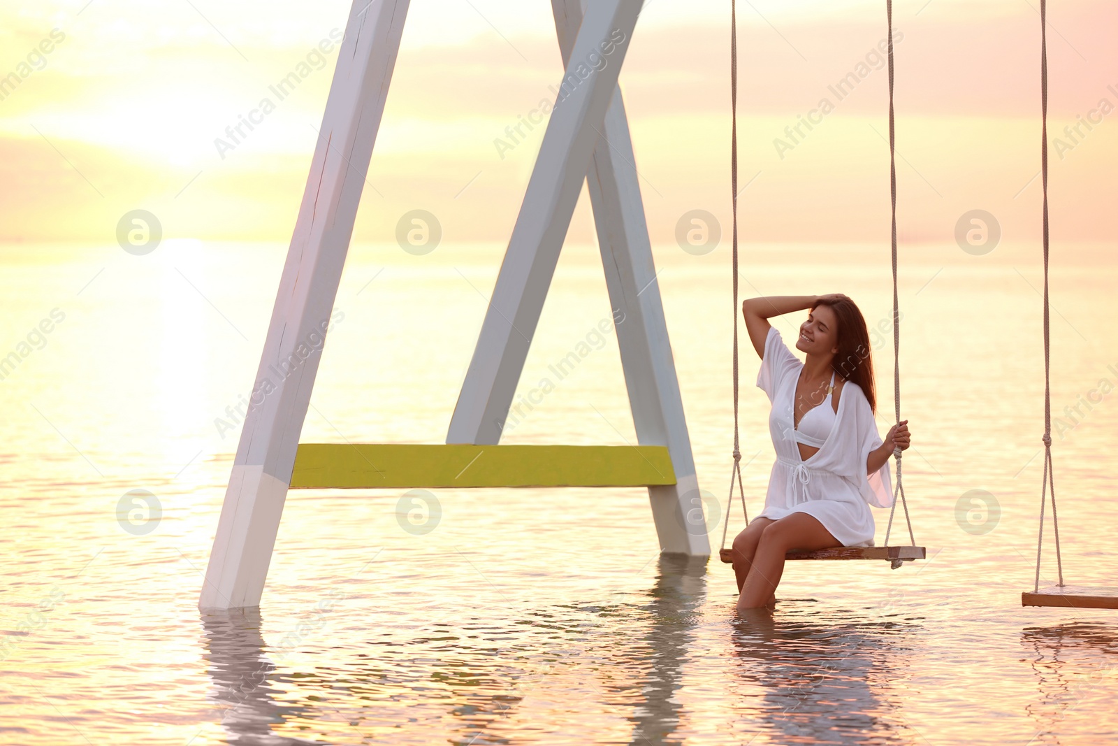 Young woman enjoying sunrise on swing over water Photo of Young woman enjoying sunrise on swing over water