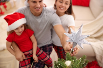 Family decorating Christmas tree indoors, focus on star topper Photo of Family decorating Christmas tree indoors, focus on star topper