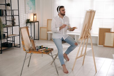Young man painting on easel with brush in artist studio Photo of Young man painting on easel with brush in artist studio