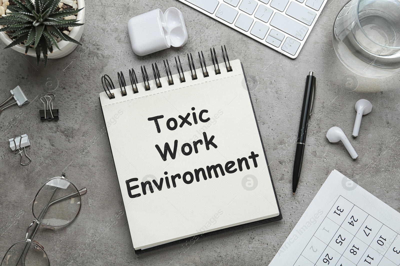 Image of Notebook with text Toxic Work Environment on grey table, flat lay